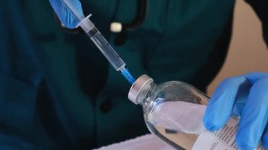 Tıbbi eldivenli bir erkek doktor şırıngaya aşı yerleştirir ve iğneye hazırlanır. Yıkama koşulları