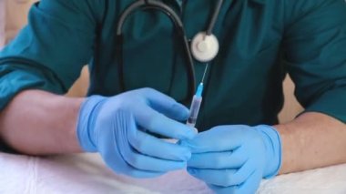 Tıbbi eldivenli bir erkek doktor şırıngaya aşı yerleştirir ve iğneye hazırlanır. Yıkama koşulları