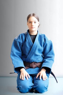 Kahverengi kemerli bir judo kızı. Genç bir judoka dövüşçüsü arka planda mavi kimonoyla poz veriyor. Japon dövüş sanatı. Dövüş sanatları eğitimi. Sağlıklı yaşam tarzı, spor anlayışı