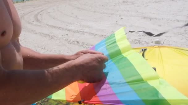 一个身材苗条的男人正在海滩上放着一只五颜六色的风筝 在河岸上进行积极的娱乐活动 成人和儿童的娱乐 — 图库视频影像