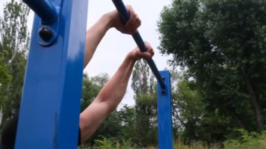 Sokaktaki oyun parkında barfiks çeken genç bir adamın portresi. Güçlü bir atlet, sağlıklı bir adam, sokakta yatay bir çubuk. Sporcu, sokak sporu.