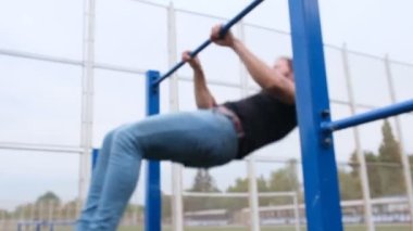 Sokaktaki oyun parkında barfiks çeken genç bir adamın portresi. Güçlü bir atlet, sağlıklı bir adam, sokakta yatay bir çubuk. Sporcu, sokak sporu.