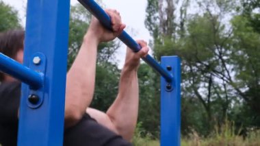 Sokaktaki oyun parkında barfiks çeken genç bir adamın portresi. Güçlü bir atlet, sağlıklı bir adam, sokakta yatay bir çubuk. Sporcu, sokak sporu.