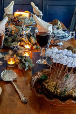 Holiday table with a rack of lamb, steamed artichoke, potatoes and on a bone China plate with candles and holiday decor. clipart