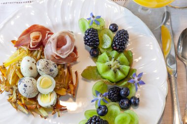 Haşhaş rengi patates yuvasında bıldırcın yumurtası, prosciutto ve dekoratif meyve..