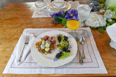 Haşhaş rengi patates yuvasında bıldırcın yumurtası, prosciutto ve dekoratif meyve..