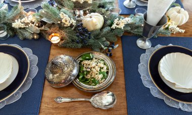 Feta cheese, spinach, and orzo in a sterling silver dish with a lid and spoon on a formal dining table. clipart