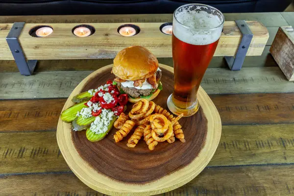 Gourmet Grilled burger with bacon and gorgonzola cheese on a brioche bun with beer and French fries.