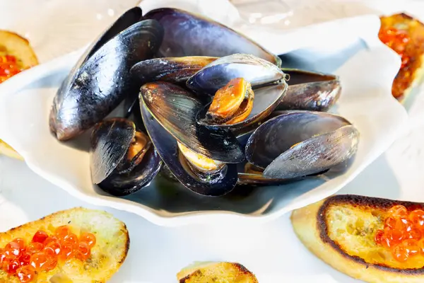 stock image Clamshell dish of mussels and garlic with red wild salmon caviar roe on pesto French bread in a nautical setting.