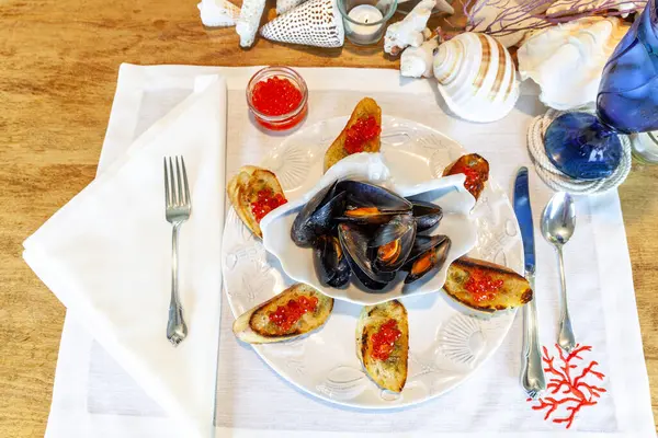 stock image Clamshell dish of mussels and garlic with red wild salmon caviar roe on pesto French bread in a nautical setting.