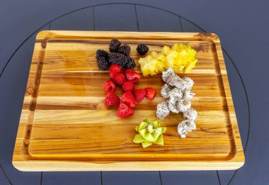 İçinde ejderha meyvesi, yıldız meyvesi, ahududu, böğürtlen ve kivi bulunan ahşap kesme tahtası..