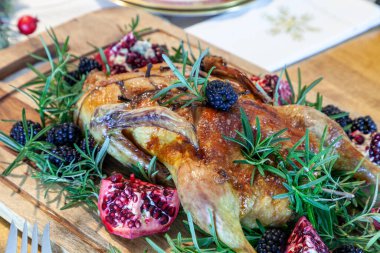 Christmas goose on a bed of rosemary with blackberries and pomegranate fruit on a cutting board. clipart