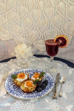 Crispy hashbrown potato nest with goat cheese and salmon lox with black berries and a blood orange mimosa on a formal table. clipart