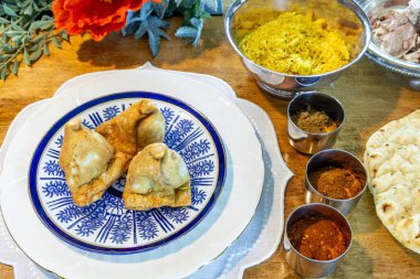 Çeşitli baharatlı Samosalar, safran pirinci, naan ekmeği ve ördek eti güzel porselen tabaklar üzerinde Hint yemeği..