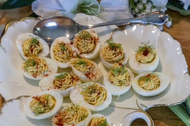 Paskalya süslemeleri, zambaklar, kelebekler, kristaller ve mumlarla süslenmiş, porselen bir tabakta içi altın dolu yumurtalar..