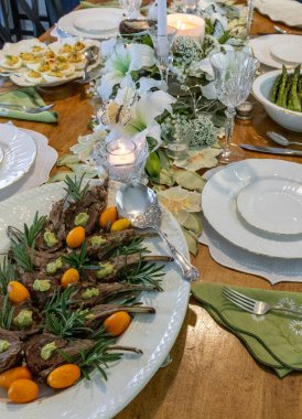 Paskalya yemeğinde kuzu eti, baharatlı yumurta ve porselen tabaklar üzerinde havuçlu kek. Paskalya süslemeli bir masa da zambaklar, kelebekler, kristaller ve mumlarla süslenmiş..