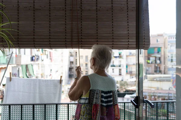 elderly woman picking up a shutter from the balcony of her home. domestic life in independent elderly people.