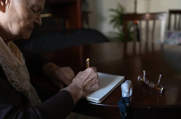 old woman writing a letter with pen and paper