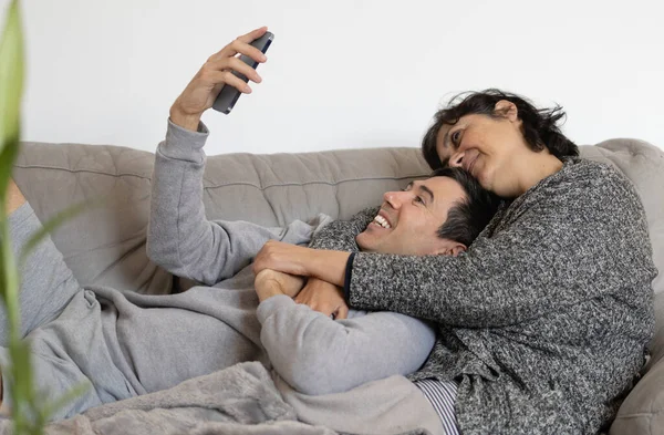 mature woman of middle eastern ethnicity and young adult caucasian man are a multiethnic couple.they are smiling happily and taking a selfie with their mobile phone.they are hugging and in love.