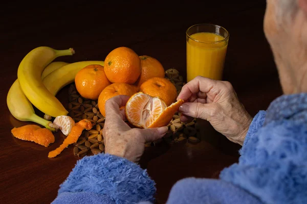 hand of an elderly woman peeling a tangerine to eat with fruit juice and banana. concept of healthy diet in the elderly and organic, biological and sustainable agriculture food.