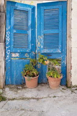 Bir avluya giriş iki eski yıpranmış ahşap kapıyla güvence altına alınır. Ek koruma olarak, iki büyük saksı erişimi engelliyor..