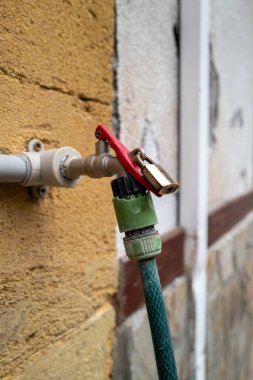 Bir ev duvarında, bahçe hortumu bağlantısı izinsiz kullanımlara karşı asma kilit ile korunur..