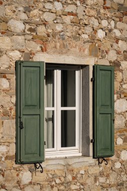Beyaz pencereli ve koyu yeşil panjurlu yaşlanmış taş bir duvar. Eski bir binanın büyüleyici ayrıntıları..