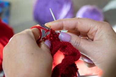 Kadın elleri şiş ve kırmızı iplikle çorap örüyor. Kırmızı ve leylak renginde demetler. Ellerini yaklaştır.