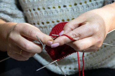 Kadın elleri şiş ve kırmızı iplikle çorap örüyor. Ellerini yaklaştır.