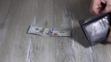 Bir adamın eli siyah deri bir cüzdandan dolar alıyor ve onları gri ahşap bir masaya koyuyor. 100 dolarlık banknotlar.