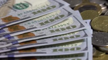 100 dolarlık banknotlara ve dünyanın çeşitli madeni paralarına yakın çekim. Bankacılık ve finansal konsept. Panoramik kamera hareketi. Sığ alan derinliği