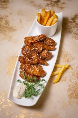 Tatlı ve ekşi soslu kanatlar susam tohumları ve beyaz bir tabakta patates kızartması..
