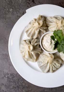 beyaz bir tabakta khinkali soslu ve gri arka planda otlar.