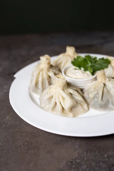 stock image khinkali on a white plate with sauce and herbs on a gray background.