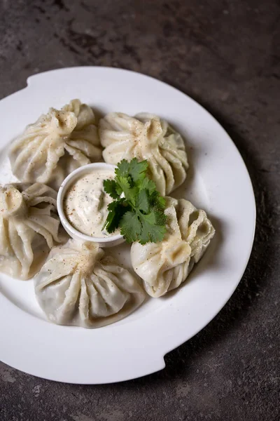 stock image top view of khinkali on a white plate with sauce and herbs on a gray background.