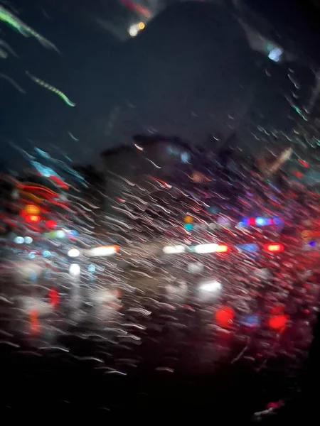 雨の中のガラス越しの夜の街の明るい光 雨の中のぼんやりとした光とボケの抽象的な背景 — ストック写真