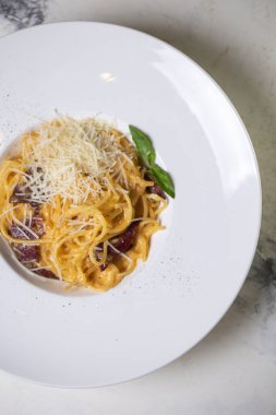 Pastırmalı, kremalı ve peynirli Carbonara makarnası bir restoranda beyaz tabakta..