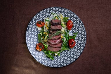 Üst manzara, domatesli ve otlu bir tabakta, sulu kesilmiş et parçaları..