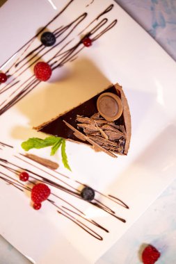 Kahve dükkanındaki lezzetli çikolatalı keki beyaz tabakta böğürtlenli görürüz..