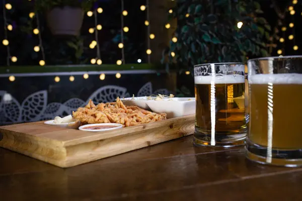 木桌上的啤酒和小吃洋葱圈 — 图库照片