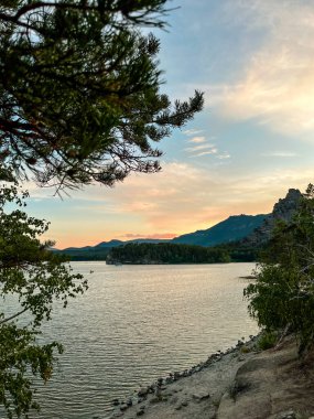 Kazakistan 'daki Borovoye tatil köyündeki göl gün batımında bir dağın arka planına karşı..