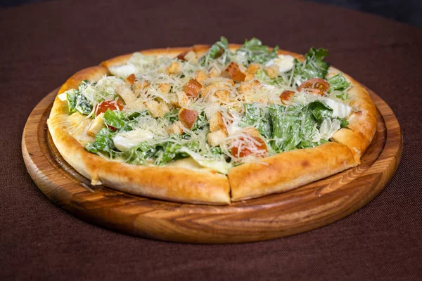 A delicious round pizza with salad, tomatoes, cheese, croutons on wooden board. Isolated on brown background, perfect for food blogs, restaurant websites, social media.