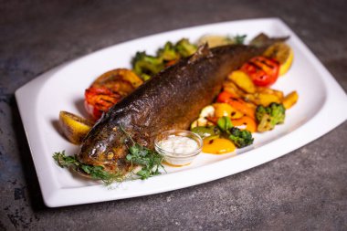 Limon ve maydanozla süslenmiş, çeşitli sebzelerle ızgara balık. Lezzetli deniz ürünleri yemeği..