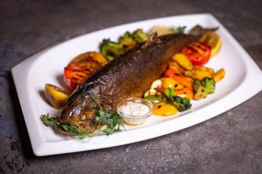 Limon ve maydanozla süslenmiş, çeşitli sebzelerle ızgara balık. Lezzetli deniz ürünleri yemeği..