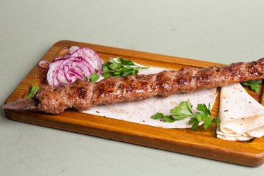 Tahta bir tahtanın üzerinde soğan halkaları ve maydanozla servis edilen lezzetli tavuk şiş kebap. Arzularını bu lezzetli yemekle tatmin et..
