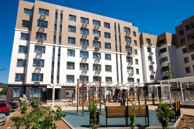 Bahçesi olan modern apartman binaları. Çağdaş tasarım, büyük pencereler, balkonlar. Salıncaklı, kaydırmalı, tırmanmalı oyun alanı.