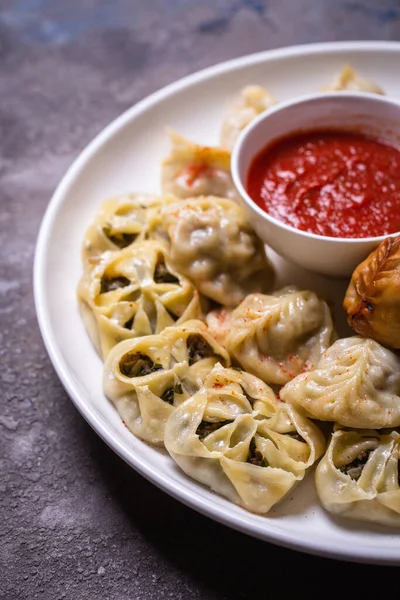 Kırmızı soslu bir tabakta servis edilen et, balkabağı ve sebzeli Özbek hamur tatlısı çeşitleri.