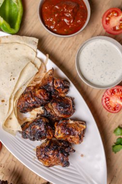 Sebze ve otlarla dolu beyaz bir tabakta pide ekmekli ciğer kebabı..