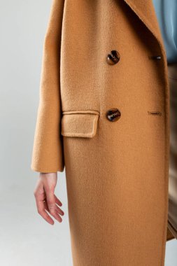 Büyük düğmeleri olan, koyu kahverengi ceketli şık bir genç kadın. Beyaz duvarın yanında poz vermek. Metin veya reklam için boşluk kopyala.