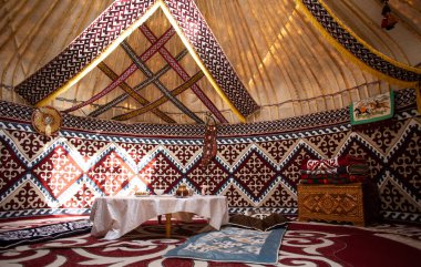 Orta Asya yurdunda keçeli halılar, mobilyalar ve masa var. Beyaz masa örtülü geleneksel göçebe konutu.